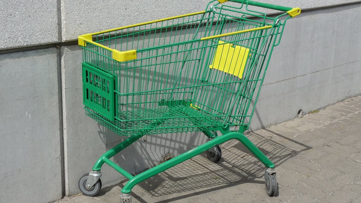 Prázdný zelený nákupní vozík u šedé zdi před supermarketem
